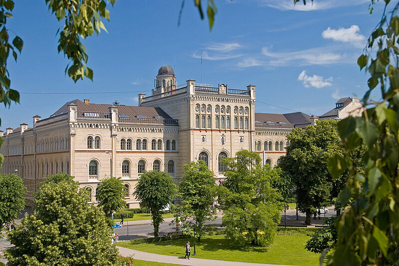 Main building of the University of Latvia on a sunny day, framed by green trees