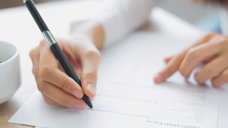 Close-up of a person filling out an application form with a pen